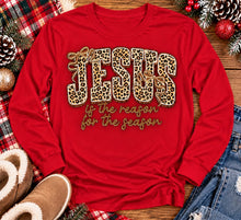 Load image into Gallery viewer, Jesus Is the Reason for the Season Christmas graphic shirt featuring bold leopard print JESUS lettering, decorative gold bows, and gold script. Faith-inspired holiday apparel available in red and black with four style options.