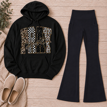 Load image into Gallery viewer, Black Just Pray graphic pullover hoodie with leopard, checkerboard, cow-print, star, and gold accents styled with black pocket flare leggings and beige slip-on shoes.
