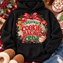 Load image into Gallery viewer, A black pullover hoodie laid flat with a large festive Christmas cookie baking graphic on the front. The design includes red bows, green pine branches, gingerbread cookies, mixing bowls, and the words “Christmas Cookie Baking Crew.