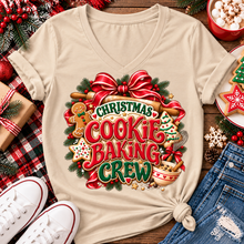 Load image into Gallery viewer, A beige V-neck t-shirt with a colorful 'Christmas Cookie Baking Crew' graphic, styled in a flat lay with jeans, white sneakers, holiday decorations, and cookies on a wooden surface.