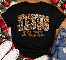 Load image into Gallery viewer, Jesus Is the Reason for the Season Christmas graphic shirt featuring bold leopard print JESUS lettering, decorative gold bows, and gold script. Faith-inspired holiday apparel available in red and black with four style options.
