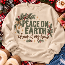 Load image into Gallery viewer, Peace on Earth Chaos at My House funny Christmas graphic apparel featuring distressed olive green lettering, rustic pine greenery, red berries and gold stars, available in sand and sport grey in short sleeve crewneck tees, V-neck tees, sweatshirts and hoodies.