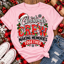 Load image into Gallery viewer, Christmas Crew Making Memories Together graphic on a pink crewneck T-shirt, featuring red lettering, colorful Christmas lights, a Santa hat, holly, and snowflakes.