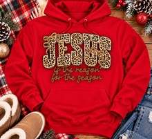 Load image into Gallery viewer, Jesus Is the Reason for the Season Christmas graphic shirt featuring bold leopard print JESUS lettering, decorative gold bows, and gold script. Faith-inspired holiday apparel available in red and black with four style options.