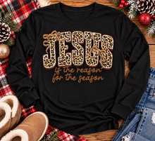 Load image into Gallery viewer, Jesus Is the Reason for the Season Christmas graphic shirt featuring bold leopard print JESUS lettering, decorative gold bows, and gold script. Faith-inspired holiday apparel available in red and black with four style options.