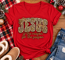 Load image into Gallery viewer, Jesus Is the Reason for the Season Christmas graphic shirt featuring bold leopard print JESUS lettering, decorative gold bows, and gold script. Faith-inspired holiday apparel available in red and black with four style options.