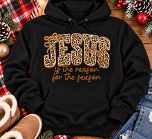 Load image into Gallery viewer, Jesus Is the Reason for the Season Christmas graphic shirt featuring bold leopard print JESUS lettering, decorative gold bows, and gold script. Faith-inspired holiday apparel available in red and black with four style options.