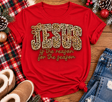Load image into Gallery viewer, Jesus Is the Reason for the Season Christmas graphic shirt featuring bold leopard print JESUS lettering, decorative gold bows, and gold script. Faith-inspired holiday apparel available in red and black with four style options.