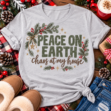 Load image into Gallery viewer, Peace on Earth Chaos at My House funny Christmas graphic apparel featuring distressed olive green lettering, rustic pine greenery, red berries and gold stars, available in sand and sport grey in short sleeve crewneck tees, V-neck tees, sweatshirts and hoodies.