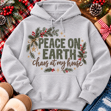 Load image into Gallery viewer, Peace on Earth Chaos at My House funny Christmas graphic apparel featuring distressed olive green lettering, rustic pine greenery, red berries and gold stars, available in sand and sport grey in short sleeve crewneck tees, V-neck tees, sweatshirts and hoodies.