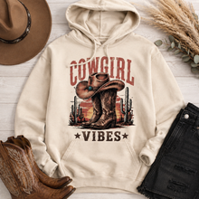 Load image into Gallery viewer, Cream Cowgirl Vibes hoodie featuring vintage cowboy boots, western cowgirl hat, cactus and desert sunset graphic in rustic brown and red tones.