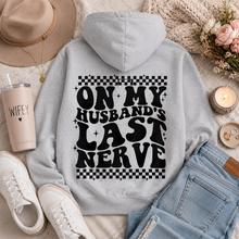 Load image into Gallery viewer, Gray graphic hoodie featuring bold black āOn My Husbandās Last Nerveā lettering with checkerboard and sparkle details on the back.
