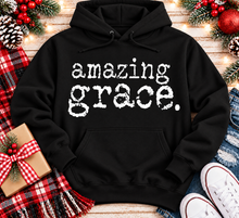 Load image into Gallery viewer, A black pullover hoodie with the words 'amazing grace.' printed in a distressed white typewriter-style font across the chest.
