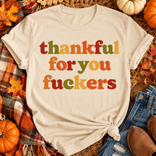 Load image into Gallery viewer, Funny Thankful for You Fuckers Thanksgiving graphic tee featuring bold retro lettering in burnt orange, mustard yellow, olive green, and rust red. Women's fall-inspired short sleeve crewneck shirt available in beige and brown, perfect for Thanksgiving and Friendsgiving.
