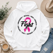 Load image into Gallery viewer, A white pullover hoodie laid flat with a pink awareness ribbon and the word 'Fight' printed on the chest, surrounded by black text reading 'Believe', 'Hope', 'Strength', 'Family', 'Love', 'Courage', 'Support', and 'Awareness'. The hoodie is styled in a flat lay with a hat, jeans, a plant, a cup of coffee, and a knit blanket on a light beige surface.
