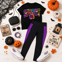 Load image into Gallery viewer, Black V-neck Halloween shirt featuring a colorful SPOOKY ghost graphic, styled with black and purple pocket leggings, white sneakers, and accessories.
