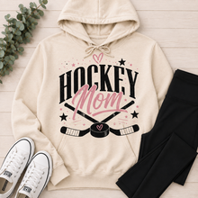 Load image into Gallery viewer, Cream Hockey Mom graphic hoodie featuring a black and pink hockey design with crossed sticks, puck, stars and heart details.
