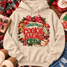 Load image into Gallery viewer, A beige pullover hoodie with a large Christmas cookie baking crew graphic, styled in a cozy holiday flat-lay with a gift box, slippers, denim, and a mug of hot chocolate.
