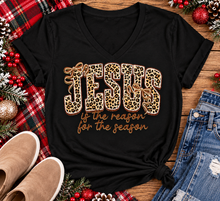 Load image into Gallery viewer, Jesus Is the Reason for the Season Christmas graphic shirt featuring bold leopard print JESUS lettering, decorative gold bows, and gold script. Faith-inspired holiday apparel available in red and black with four style options.
