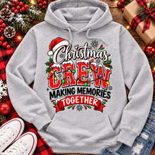 Load image into Gallery viewer, Christmas Crew Making Memories Together graphic on a pink crewneck T-shirt, featuring red lettering, colorful Christmas lights, a Santa hat, holly, and snowflakes.
