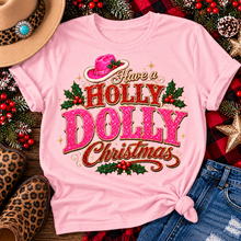 Load image into Gallery viewer, Have a Holly Dolly Christmas western graphic shirt featuring pink and red glitter-inspired lettering, a festive pink cowgirl hat, gold accents, and Christmas holly berries. Available in beige and pink in short sleeve crewneck, V-neck, long sleeve crewneck, and hoodie styles.
