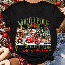 Load image into Gallery viewer, North Pole Christmas Tree Farm vintage holiday graphic shirt featuring a red pickup truck carrying Christmas trees, snowy evergreen trees, rustic farmhouse scenery, festive red bows, and distressed green lettering reading North Pole Christmas Tree Farm Always Fresh. Available in beige and black in short sleeve crewneck, V-neck, long sleeve crewneck, and hoodie styles.
