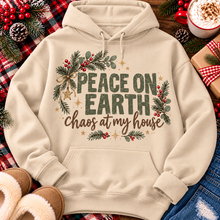 Load image into Gallery viewer, Peace on Earth Chaos at My House funny Christmas graphic apparel featuring distressed olive green lettering, rustic pine greenery, red berries and gold stars, available in sand and sport grey in short sleeve crewneck tees, V-neck tees, sweatshirts and hoodies.
