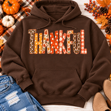 Load image into Gallery viewer, Brown Thankful fall graphic hoodie with orange floral, plaid and polka dot patchwork lettering, styled with jeans and autumn decorations.
