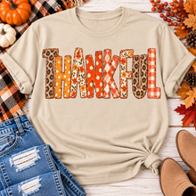 Load image into Gallery viewer, Beige short sleeve crewneck graphic tee with Thankful lettering in orange and neutral fall patterns, styled with distressed jeans.
