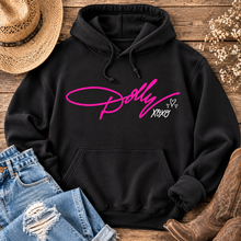 Load image into Gallery viewer, Black Dolly XOXO graphic hoodie featuring bright pink Dolly script with white XOXO and heart details, styled with distressed jeans and cowboy boots.
