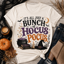 Load image into Gallery viewer, Beige Halloween graphic tee with It’s All Just a Bunch of Hocus Pocus lettering, cauldron, spell books, witch hat and bats.
