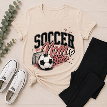 Load image into Gallery viewer, Cream crewneck Soccer Mom graphic tee featuring pink lettering, soccer ball, goal and leopard print accents.

